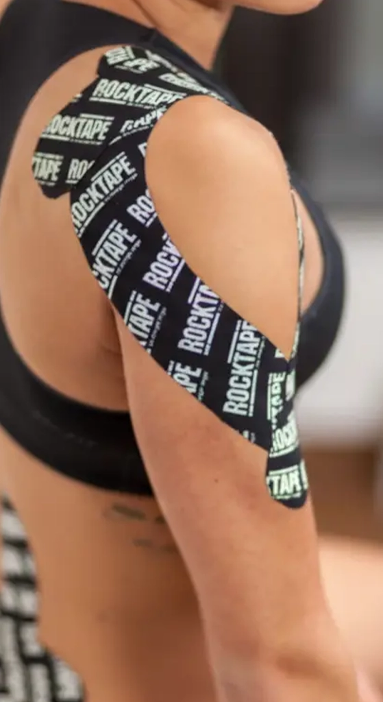 Person wearing RockTape kinesiology tape applied across the shoulder and upper arm for support and movement therapy.